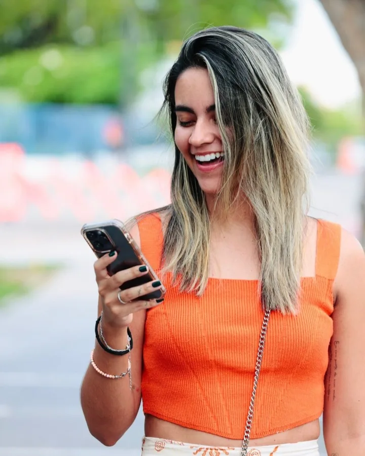 Karoll Andrade, sócia da AND.mkt, sorrindo enquanto olha o celular na rua