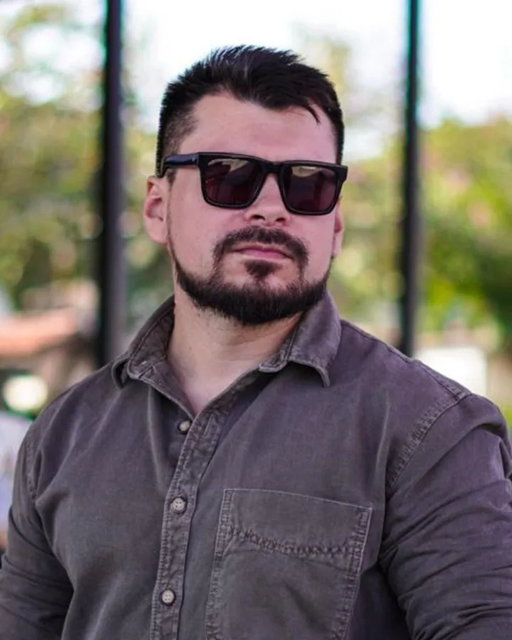 Anderson Souza, sócio da AND.mkt, de óculos escuros e camisa cinza ao ar livre